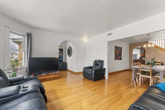 living area featuring arched walkways, visible vents, light wood finished floors, and baseboards