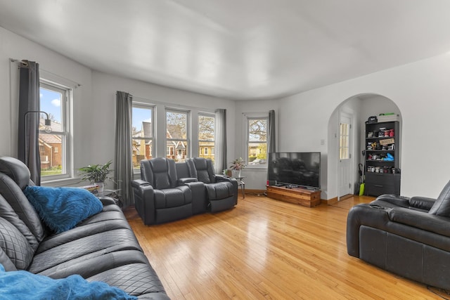 living room featuring arched walkways, light wood-style floors, and baseboards
