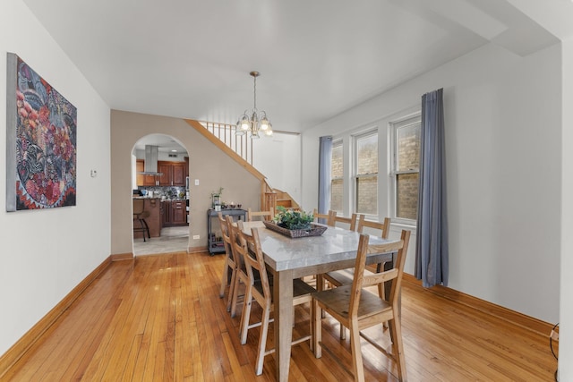 dining space featuring stairs, a chandelier, light wood-type flooring, arched walkways, and baseboards
