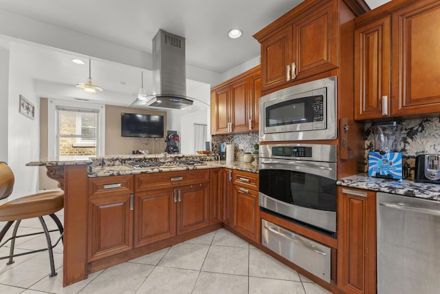 kitchen featuring a peninsula, island exhaust hood, a warming drawer, backsplash, and appliances with stainless steel finishes