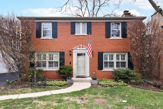 colonial house featuring brick siding, a front lawn, and a chimney