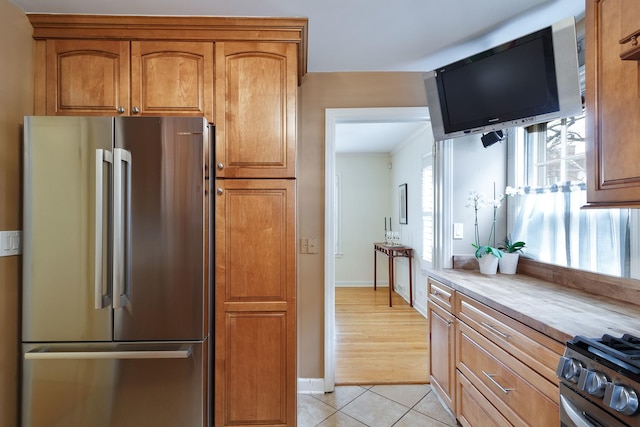 kitchen with brown cabinetry, light tile patterned floors, appliances with stainless steel finishes, light countertops, and baseboards