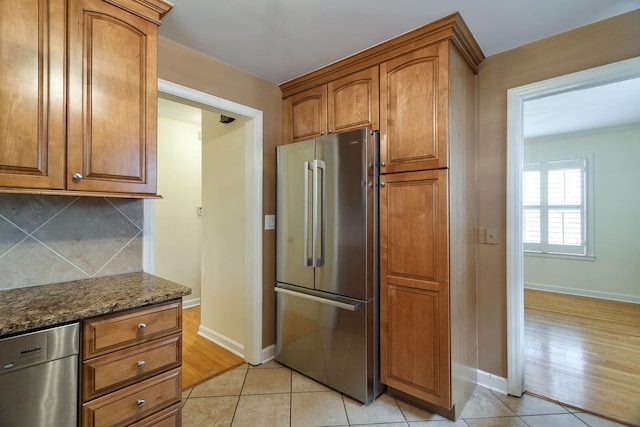 kitchen with dark stone counters, brown cabinets, decorative backsplash, stainless steel appliances, and baseboards