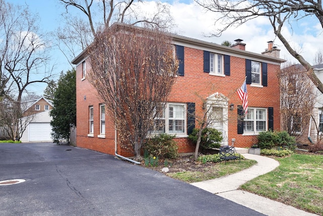 colonial house with a chimney, brick siding, an outbuilding, and a detached garage