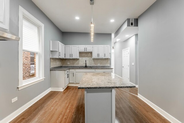 kitchen featuring wood finished floors, a center island, decorative backsplash, and a sink