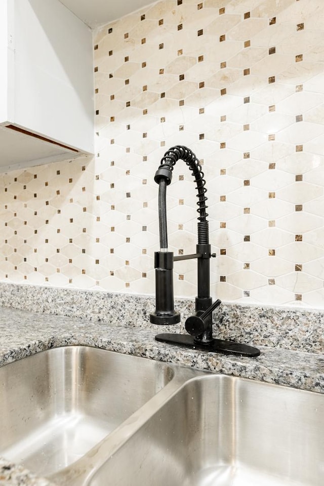 room details with light stone countertops, white cabinetry, decorative backsplash, and a sink