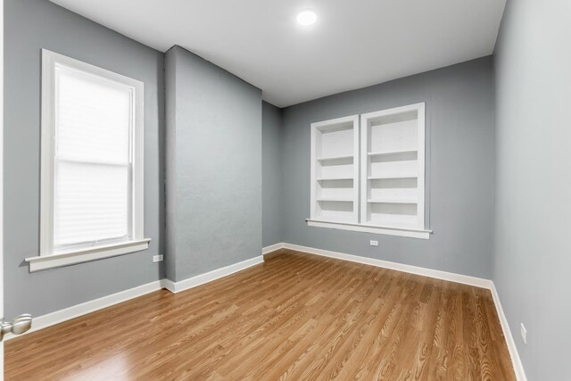 spare room with wood finished floors, built in features, and baseboards