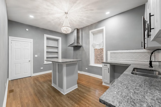 kitchen featuring wall chimney range hood, light stone counters, wood finished floors, and a sink