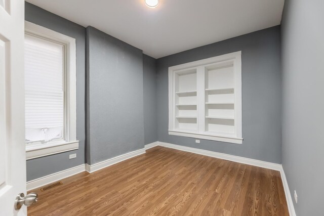 unfurnished room with baseboards, built in features, wood finished floors, and visible vents