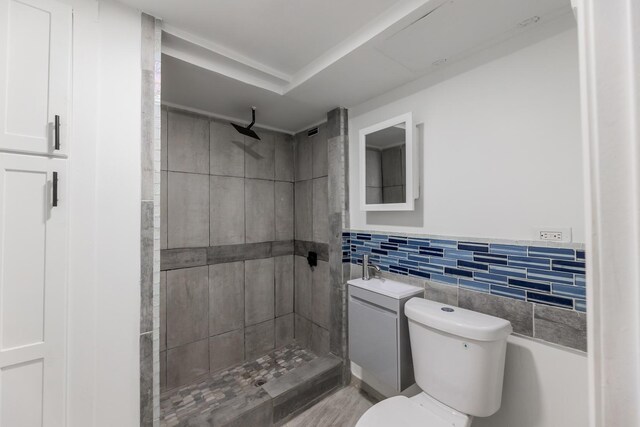 full bath with a tile shower, tile walls, toilet, and a sink