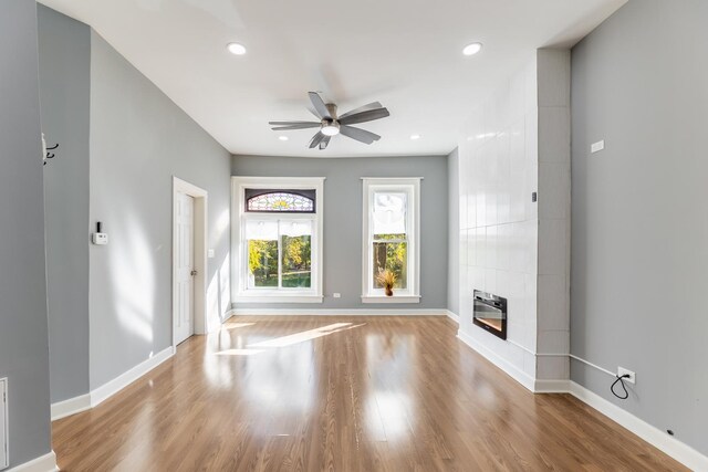 unfurnished living room with ceiling fan, baseboards, wood finished floors, and a tiled fireplace