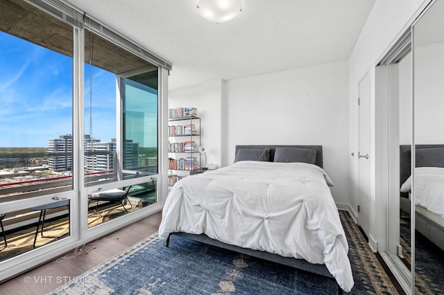 bedroom with a wall of windows, a view of city, and wood finished floors