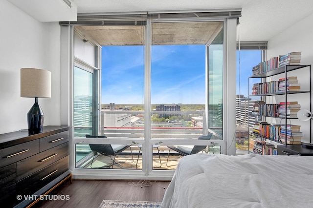 bedroom with floor to ceiling windows, wood finished floors, and a view of city