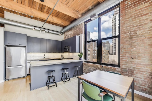 kitchen featuring brick wall, appliances with stainless steel finishes, tasteful backsplash, wooden ceiling, and light wood-style flooring