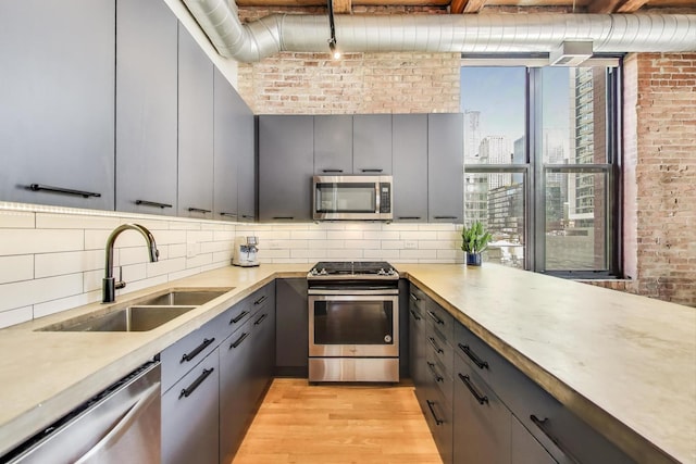 kitchen with stainless steel appliances, brick wall, gray cabinetry, and a sink