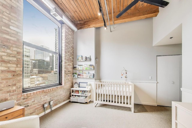 carpeted bedroom featuring wooden ceiling, baseboards, beam ceiling, and brick wall