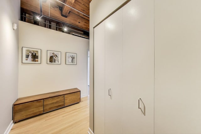 hall featuring light wood-style floors, baseboards, and beam ceiling