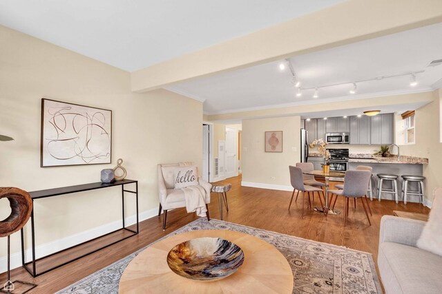 living area with baseboards, ornamental molding, and wood finished floors
