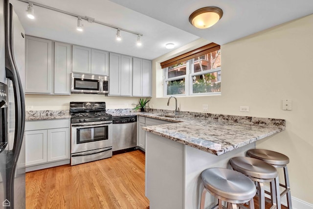 kitchen featuring a kitchen breakfast bar, appliances with stainless steel finishes, light stone countertops, a sink, and a peninsula