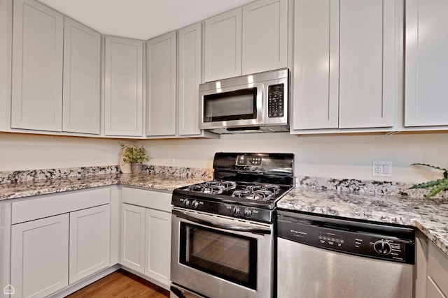 kitchen with stainless steel appliances, light stone countertops, and light wood-type flooring