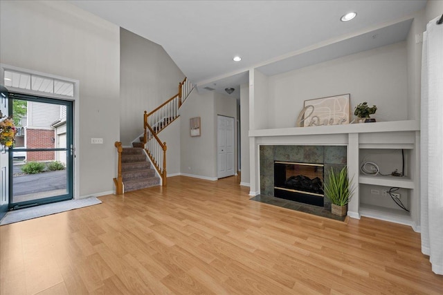 unfurnished living room featuring stairway, wood finished floors, a tile fireplace, baseboards, and recessed lighting