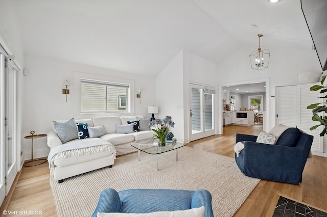 living room featuring baseboards, an inviting chandelier, high vaulted ceiling, and light wood-style flooring