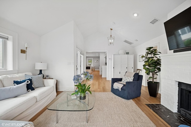 living area with vaulted ceiling, visible vents, wood finished floors, and a brick fireplace