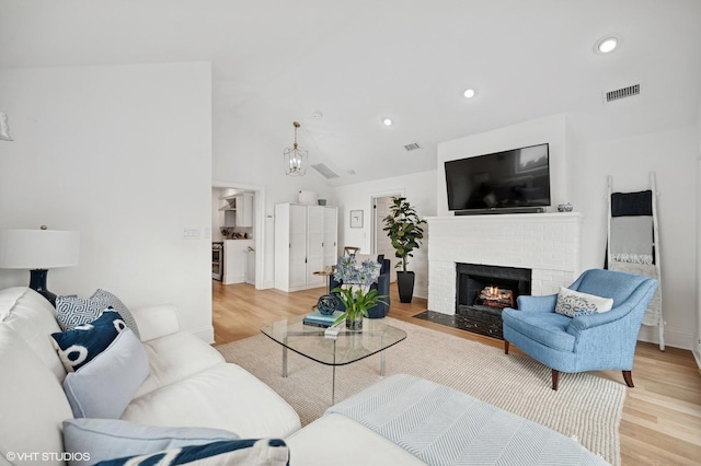 living room featuring high vaulted ceiling, visible vents, recessed lighting, a fireplace, and light wood finished floors