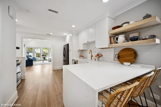 kitchen featuring a sink, a peninsula, light wood-style floors, white cabinets, and appliances with stainless steel finishes