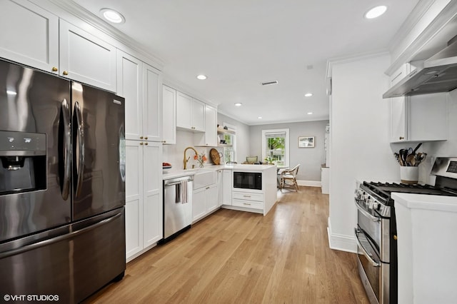 kitchen with a peninsula, a sink, baseboards, black appliances, and wall chimney range hood