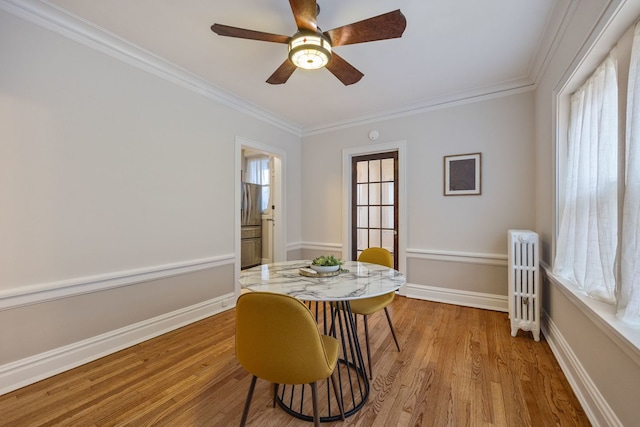 dining room featuring radiator heating unit, light wood-type flooring, crown molding, baseboards, and ceiling fan