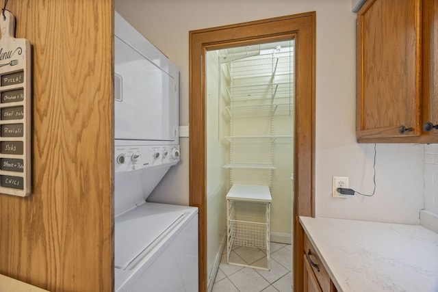 laundry room featuring stacked washer / drying machine, light tile patterned floors, and cabinet space