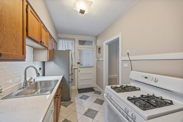 kitchen with a sink, freestanding refrigerator, backsplash, white range with gas cooktop, and brown cabinetry