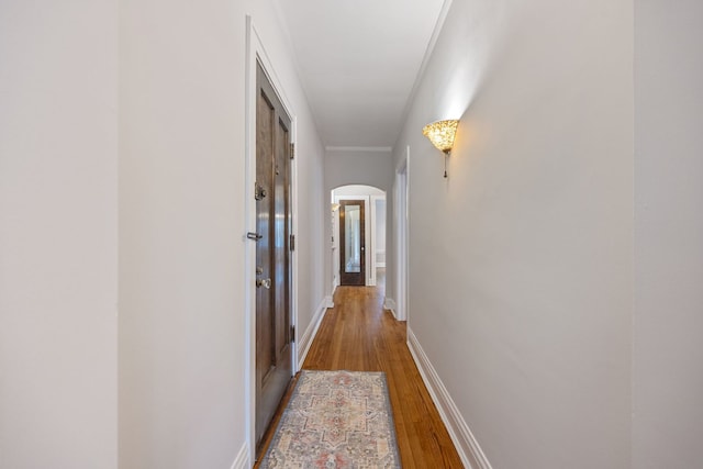corridor featuring baseboards, wood finished floors, and arched walkways