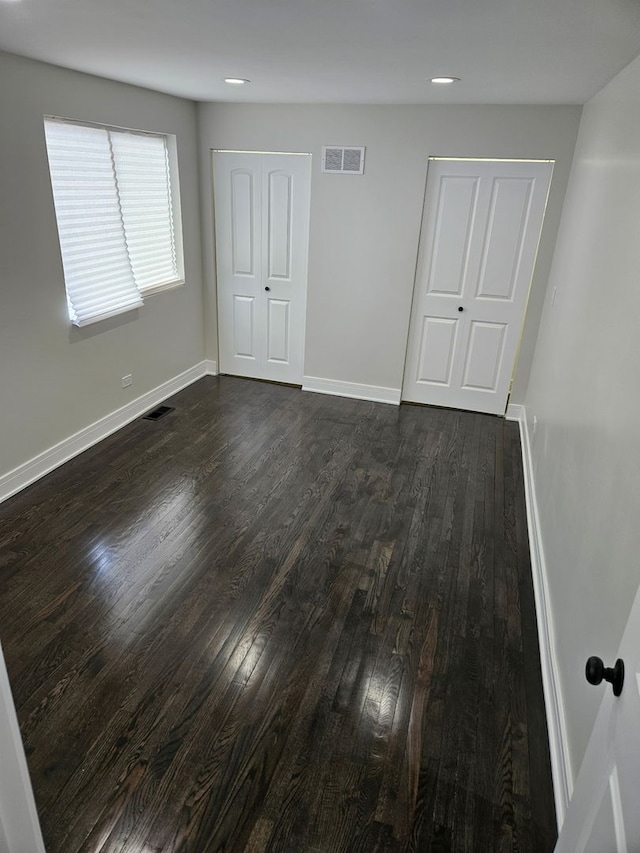 unfurnished bedroom with baseboards, dark wood finished floors, and visible vents