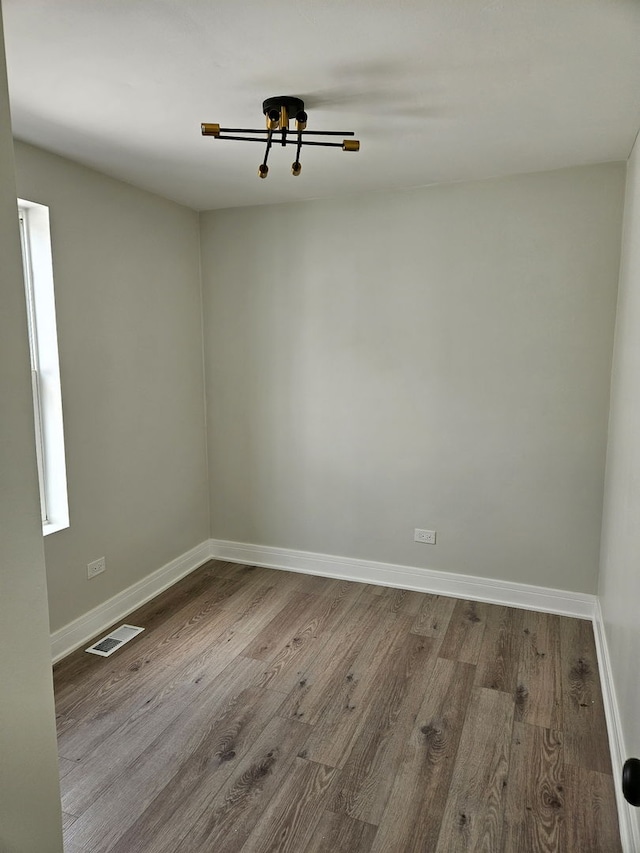 unfurnished room with baseboards, visible vents, and wood finished floors