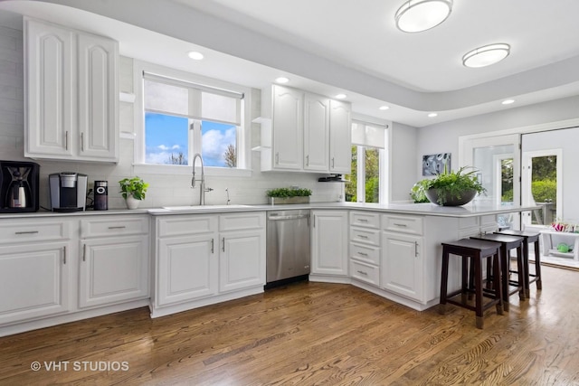 kitchen featuring decorative backsplash, a peninsula, wood finished floors, a sink, and dishwasher