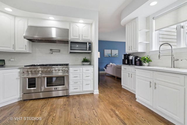 kitchen with white cabinets, appliances with stainless steel finishes, a sink, wall chimney exhaust hood, and decorative backsplash