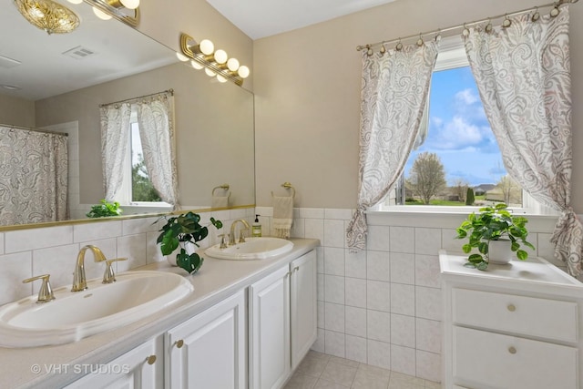 bathroom featuring visible vents, a sink, double vanity, and tile walls