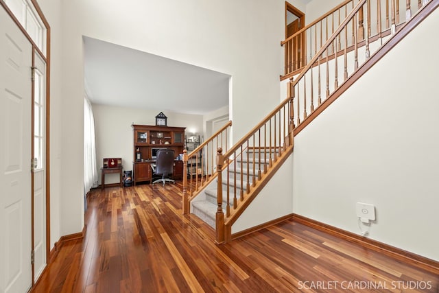 entryway with baseboards, wood finished floors, a towering ceiling, and stairs