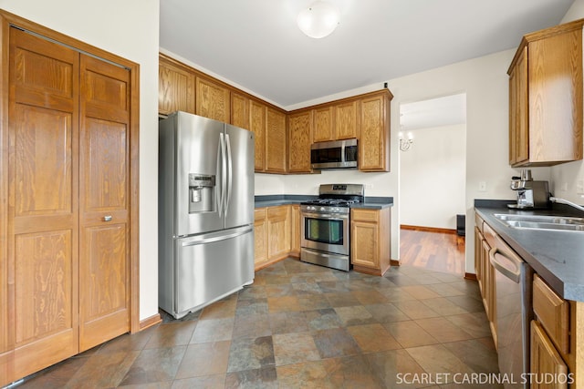 kitchen with dark countertops, a sink, brown cabinets, stainless steel appliances, and baseboards