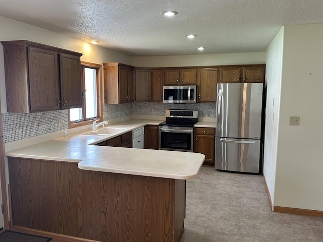 kitchen with a textured ceiling, decorative backsplash, stainless steel appliances, light countertops, and a peninsula