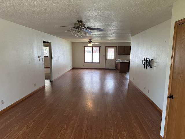 unfurnished living room featuring dark wood-type flooring, a textured ceiling, a ceiling fan, and baseboards