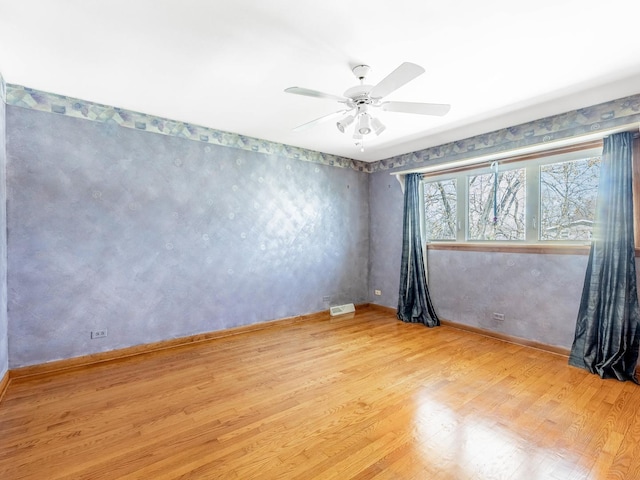 empty room with wood finished floors, baseboards, a ceiling fan, and visible vents