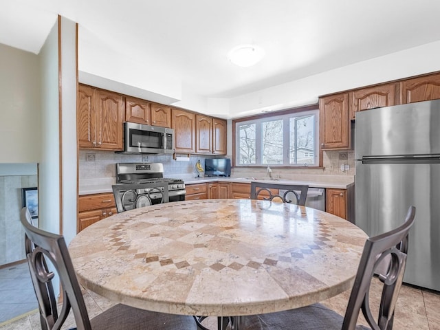 kitchen featuring tasteful backsplash, a sink, brown cabinets, light countertops, and appliances with stainless steel finishes
