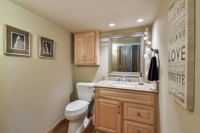 half bath with wood finished floors, vanity, baseboards, toilet, and recessed lighting