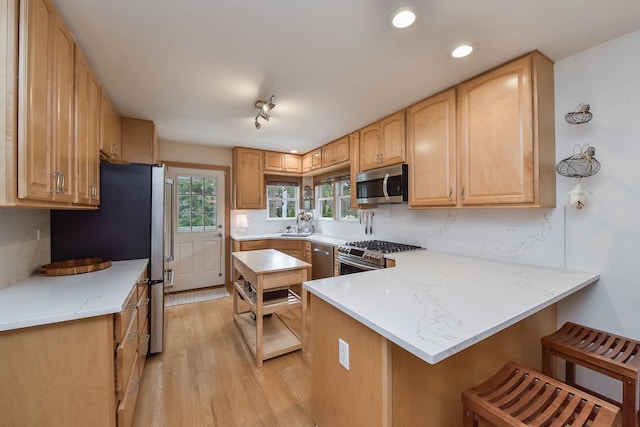 kitchen featuring a kitchen breakfast bar, appliances with stainless steel finishes, a peninsula, light wood-style floors, and recessed lighting