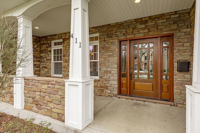 entrance to property with a porch and stone siding