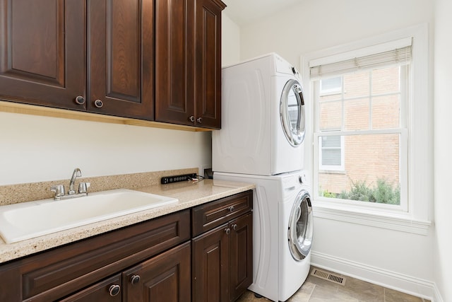 laundry area featuring visible vents, a healthy amount of sunlight, a sink, stacked washing maching and dryer, and cabinet space