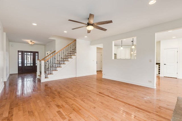 unfurnished living room with stairway, a ceiling fan, light wood-style floors, baseboards, and recessed lighting